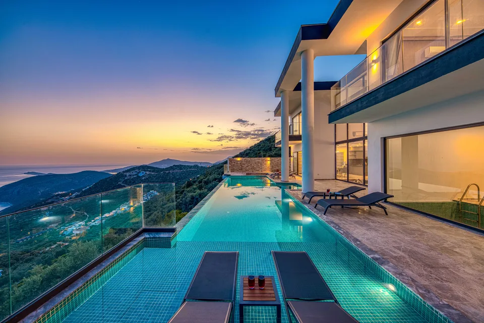 An infinity pool running along a modern villa toward the sea at sunset